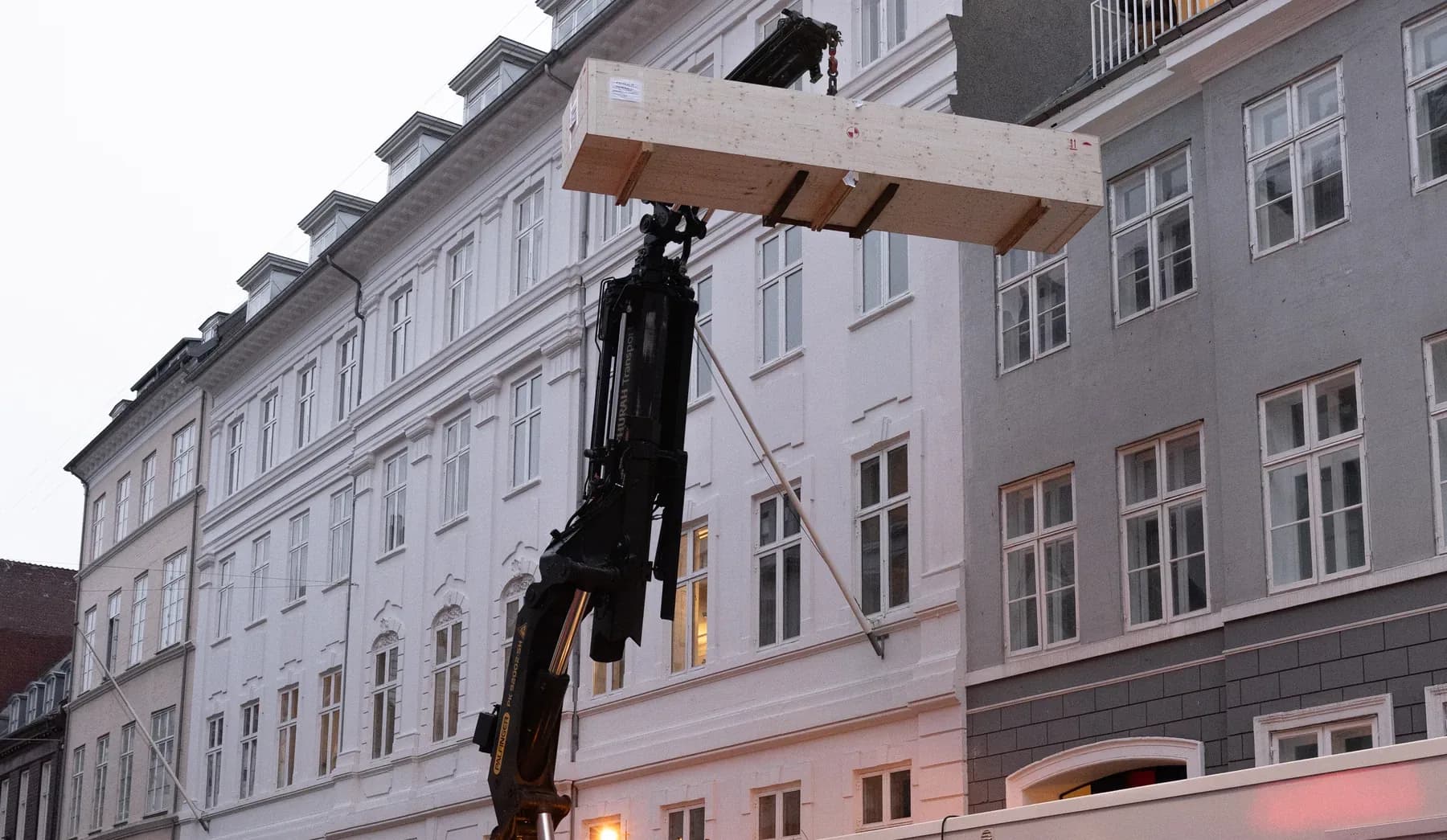 Pakke med gulvplanker løftes ind med kran foran en københavnsk facade